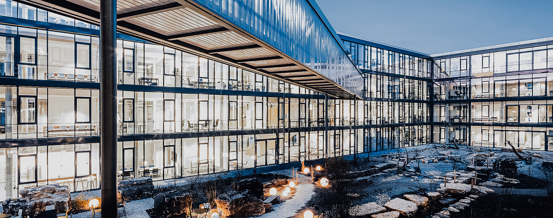 Moderno edificio de oficinas de Kärcher con grandes ventanales de cristal que dan a un patio iluminado con senderos de piedra.