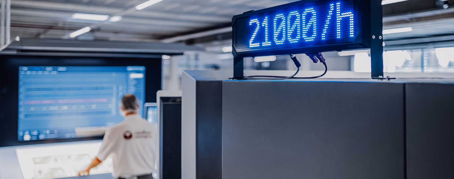 Digital display showing 21000/h above a large industrial machine with a blurred person in background.