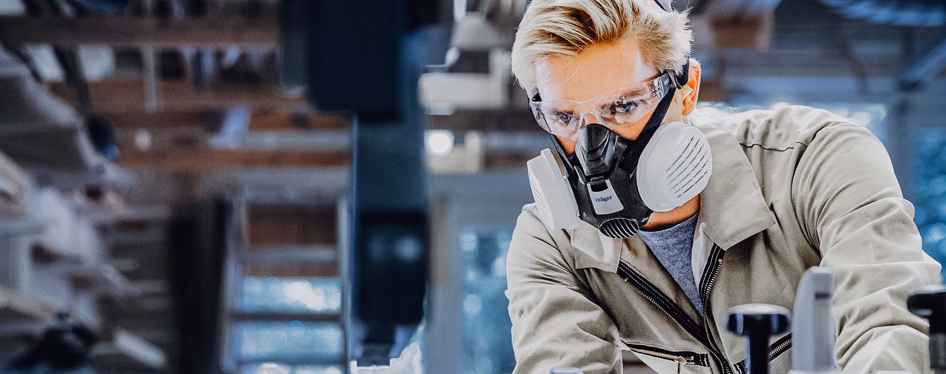 Worker wearing protective goggles and mask operating machinery in a workshop.