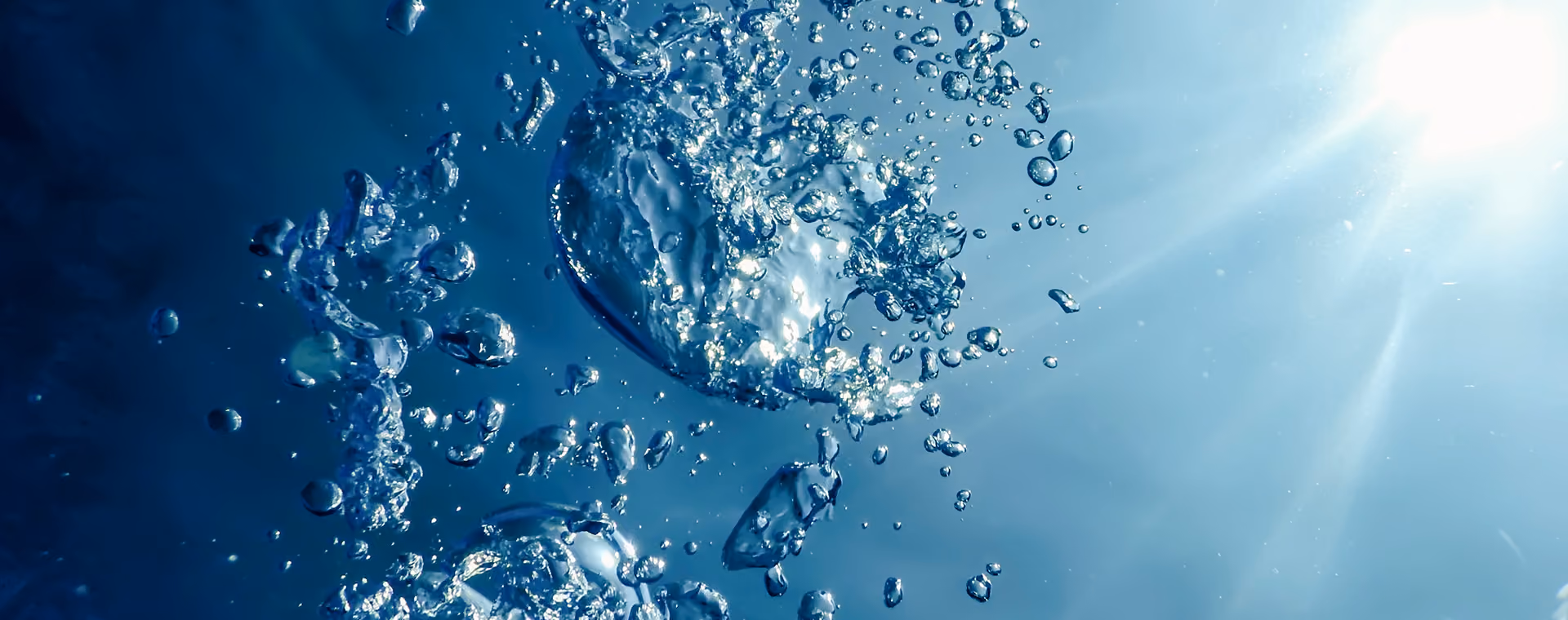 Unter Wasser aufsteigende Blasen mit Sonnenlicht, das durch klares blaues Wasser scheint.