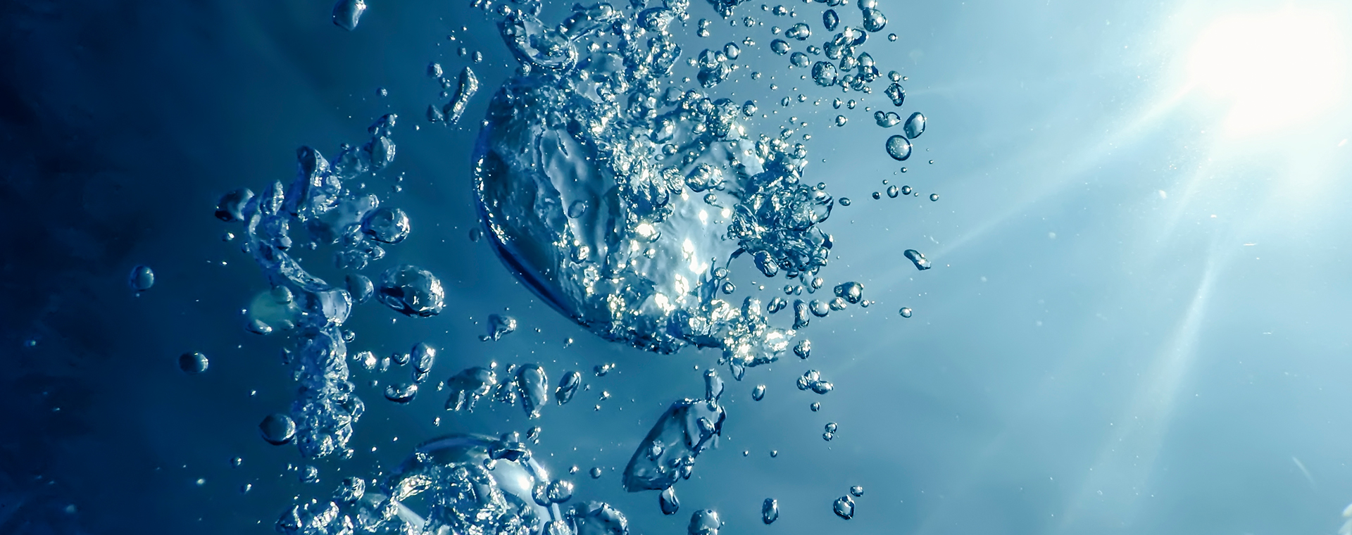 Bubbles rising underwater with sunlight shining through clear blue water.