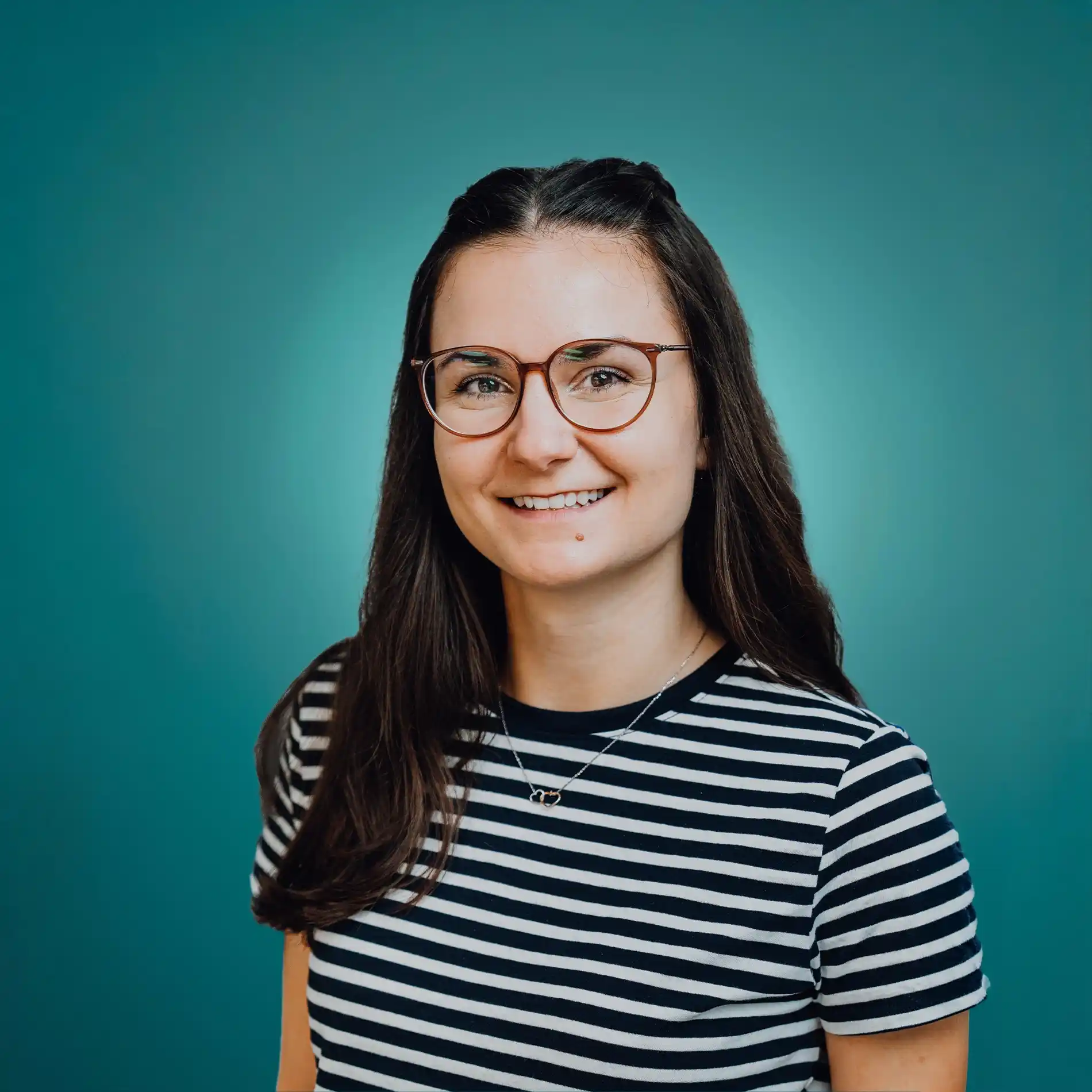 Smiling woman with long dark hair, glasses, and a striped black and white shirt against a teal background.