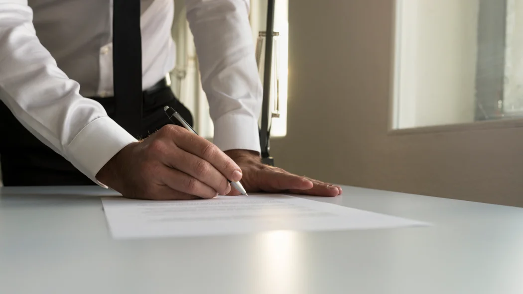 Gros plan sur un commissaire de justice signant un acte juridique officiel sur son bureau, illustrant la rédaction et la délivrance d'un commandement de payer pour loyer impayé.