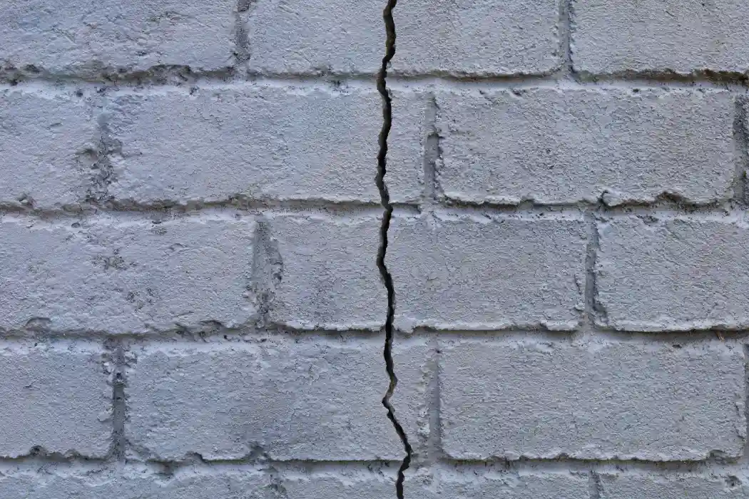 Fissure verticale traversant un mur de briques peintes, désordre typique du retrait-gonflement des sols argileux