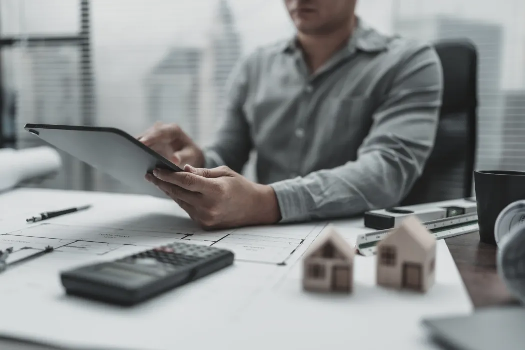 Un administrateur judiciaire ou expert comptable analysant la situation financière et les plans d'une copropriété sur une tablette numérique, entouré d'une calculatrice et de maquettes d'immeubles.