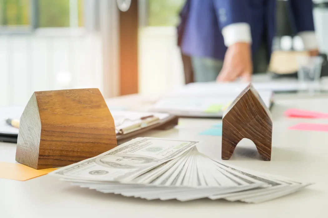 Maquettes d'immeubles en bois et liasse de billets posées sur un bureau, illustrant la planification financière et l'estimation des charges du budget prévisionnel de copropriété.