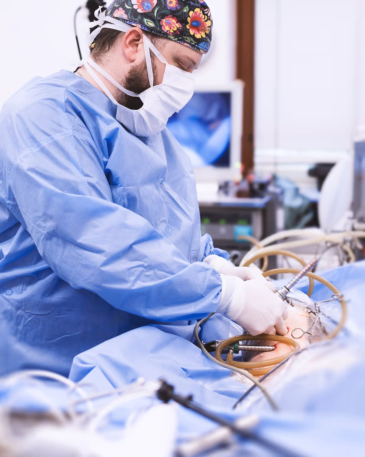 Chirurg v modrém oblečení s květovanou čepicí provádí laparoskopickou operaci pacienta.