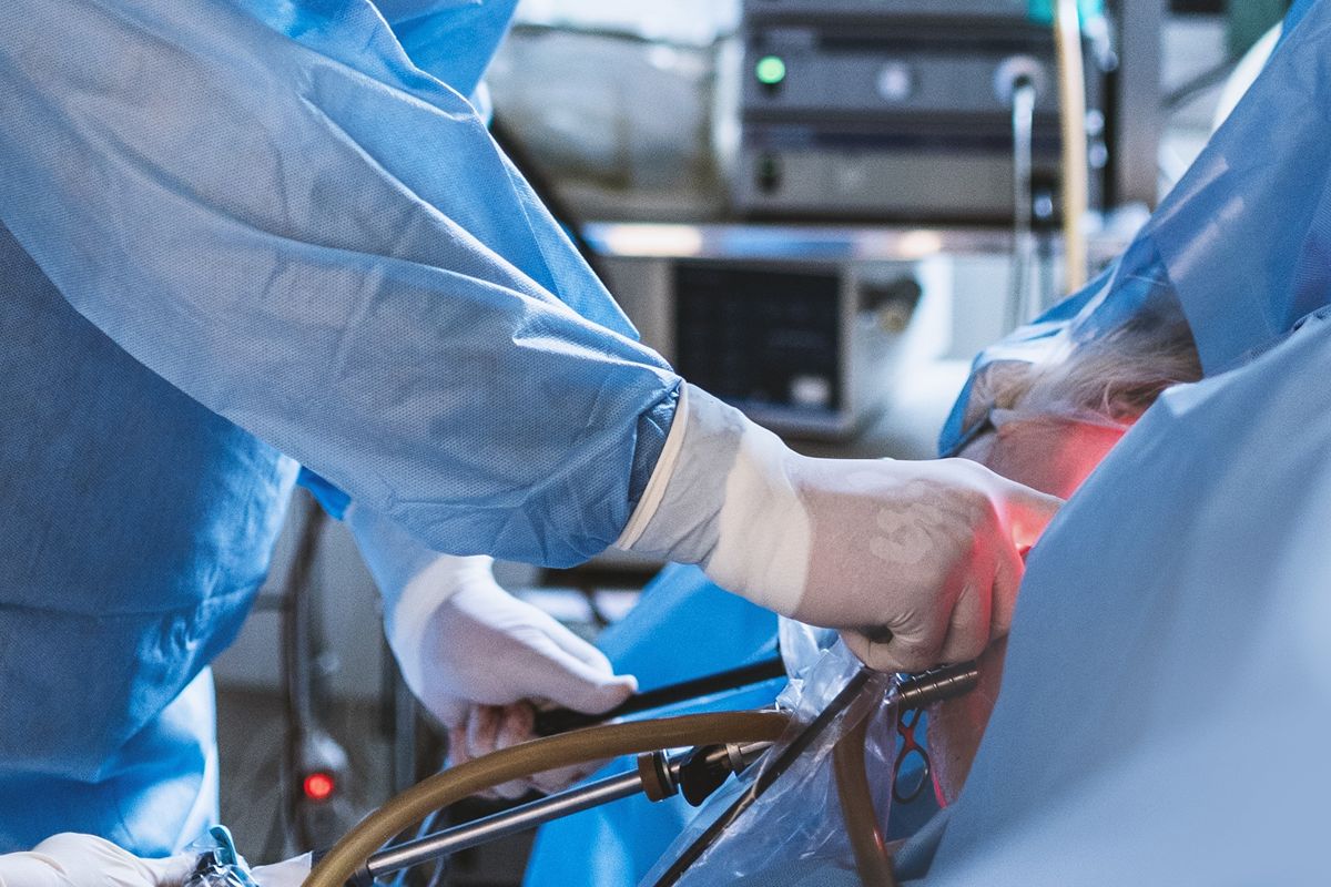 Chirurgové v modrých ochranných pláštích a rukavicích provádějí laparoskopickou operaci za použití chirurgických nástrojů a osvětlovacího zařízení.