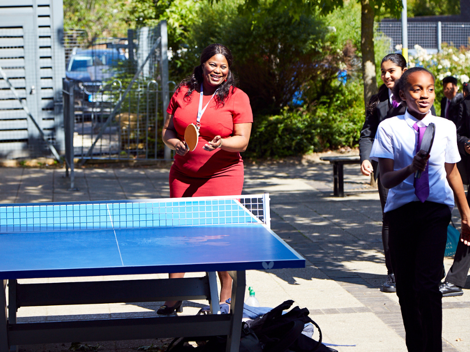 Woman in a red dress playing table tennis outdoors with a student at a Now Teach event.