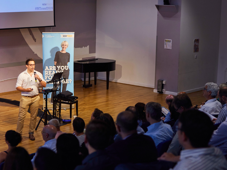 Man speaking to a seated audience at a Now Teach conference, with a banner reading 'Are You Ready For Change?' beside him.
