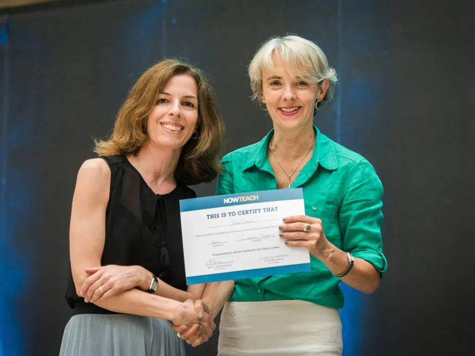 Two women smiling, shaking hands, one holding a certificate from Now Teach.
