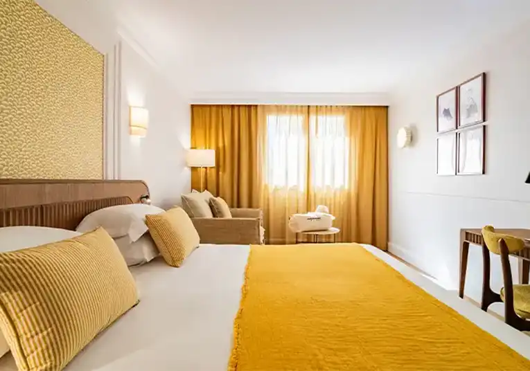 Modern bedroom with double bed, yellow cushions, beige sofa, floor lamp and large windows with yellow curtains.