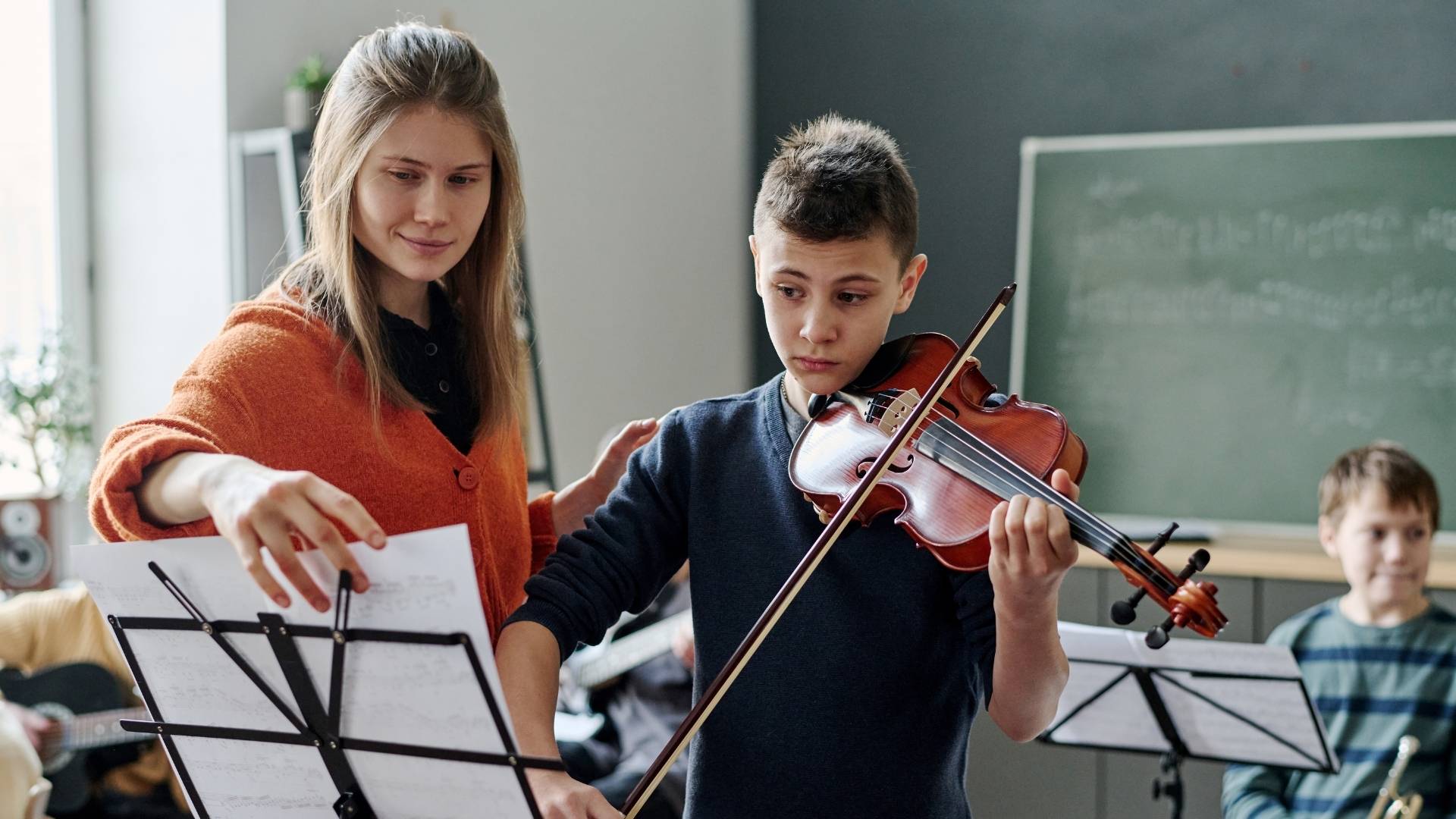 Musiklehrerin unterrichtet einen Jungen mit Geige am Notenständer