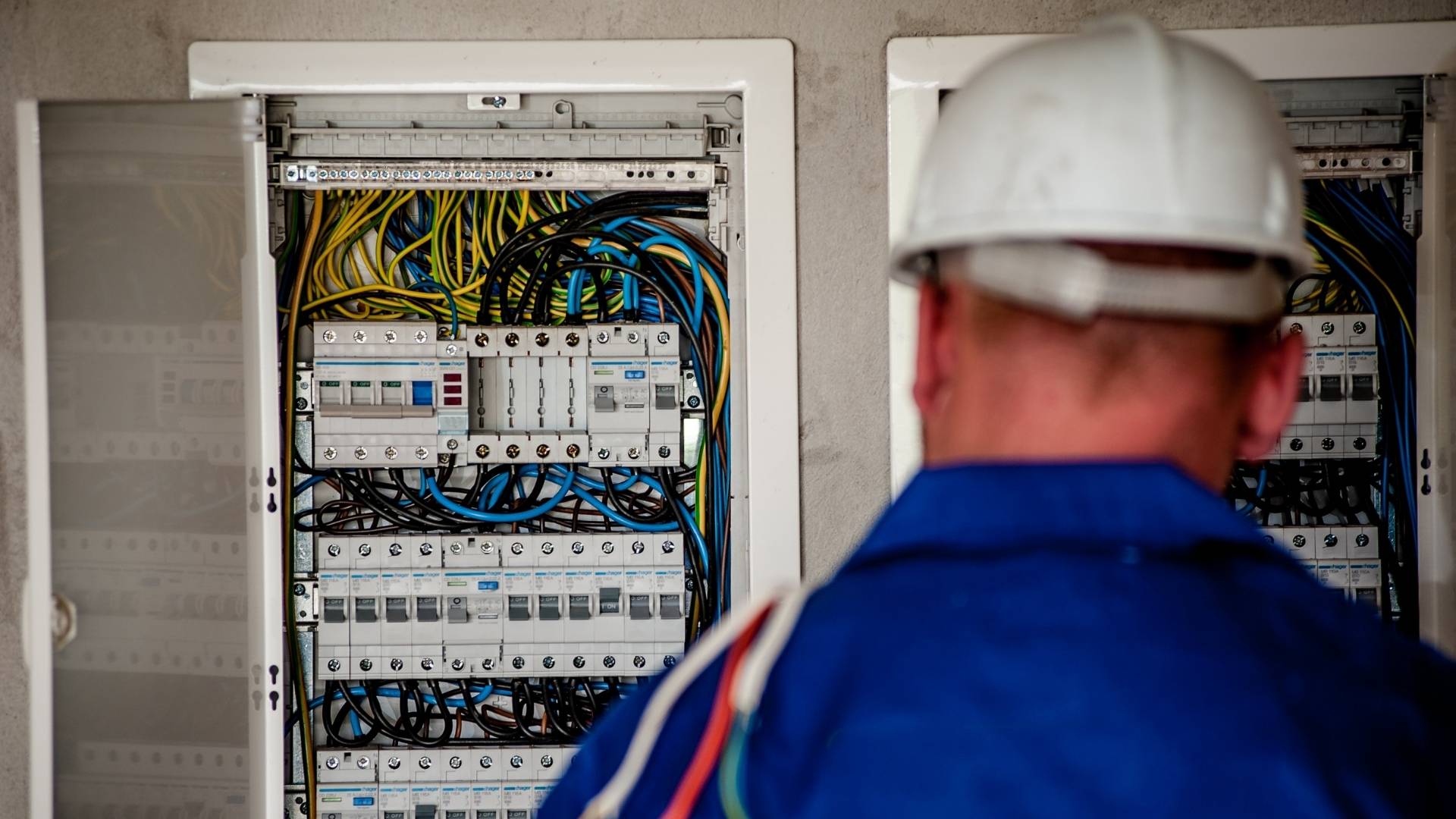 Servicetechniker mit Helm vor einem geöffneten Sicherungskasten