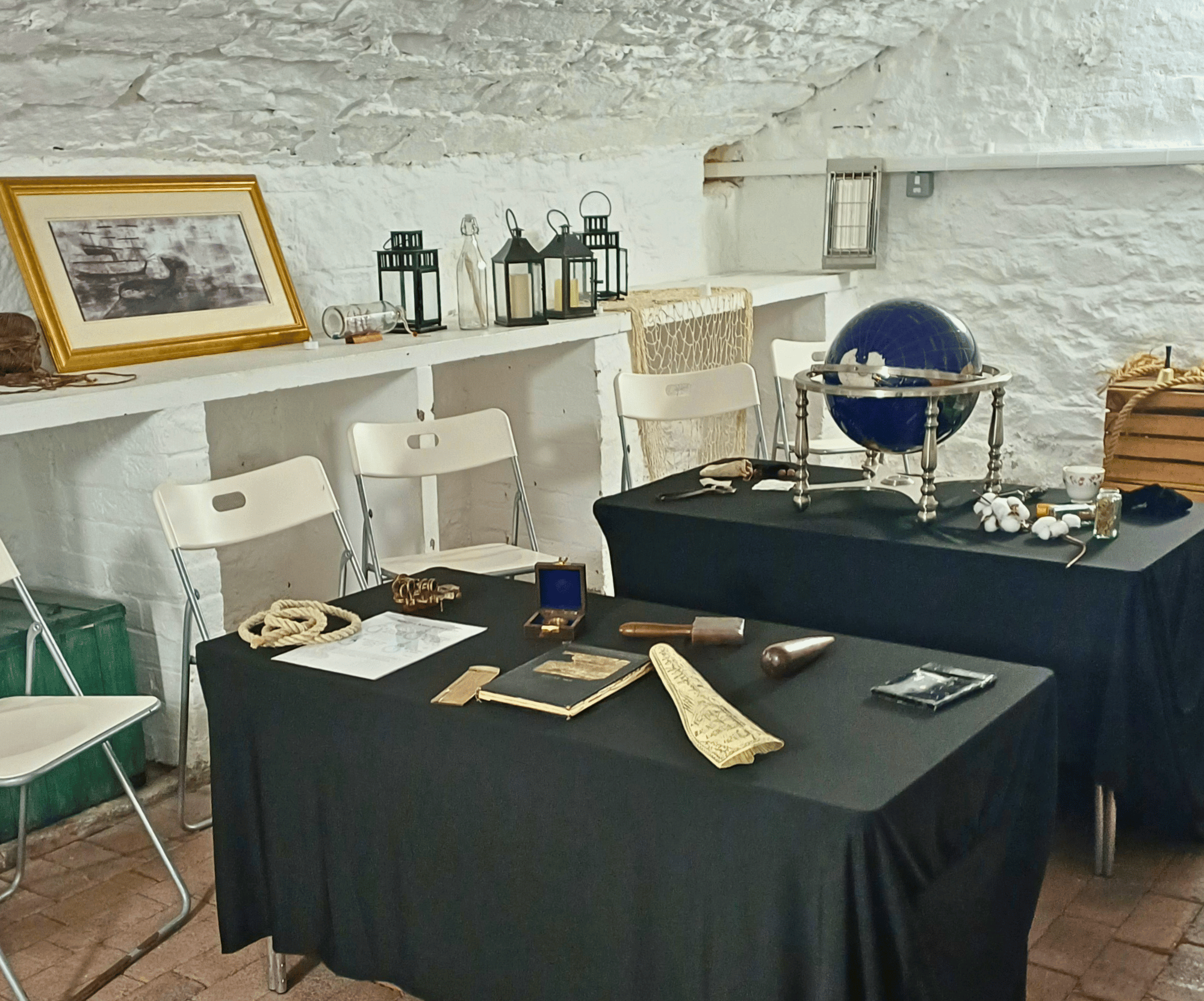 Room with black-clothed tables displaying antique items and a blue globe, against white brick walls.