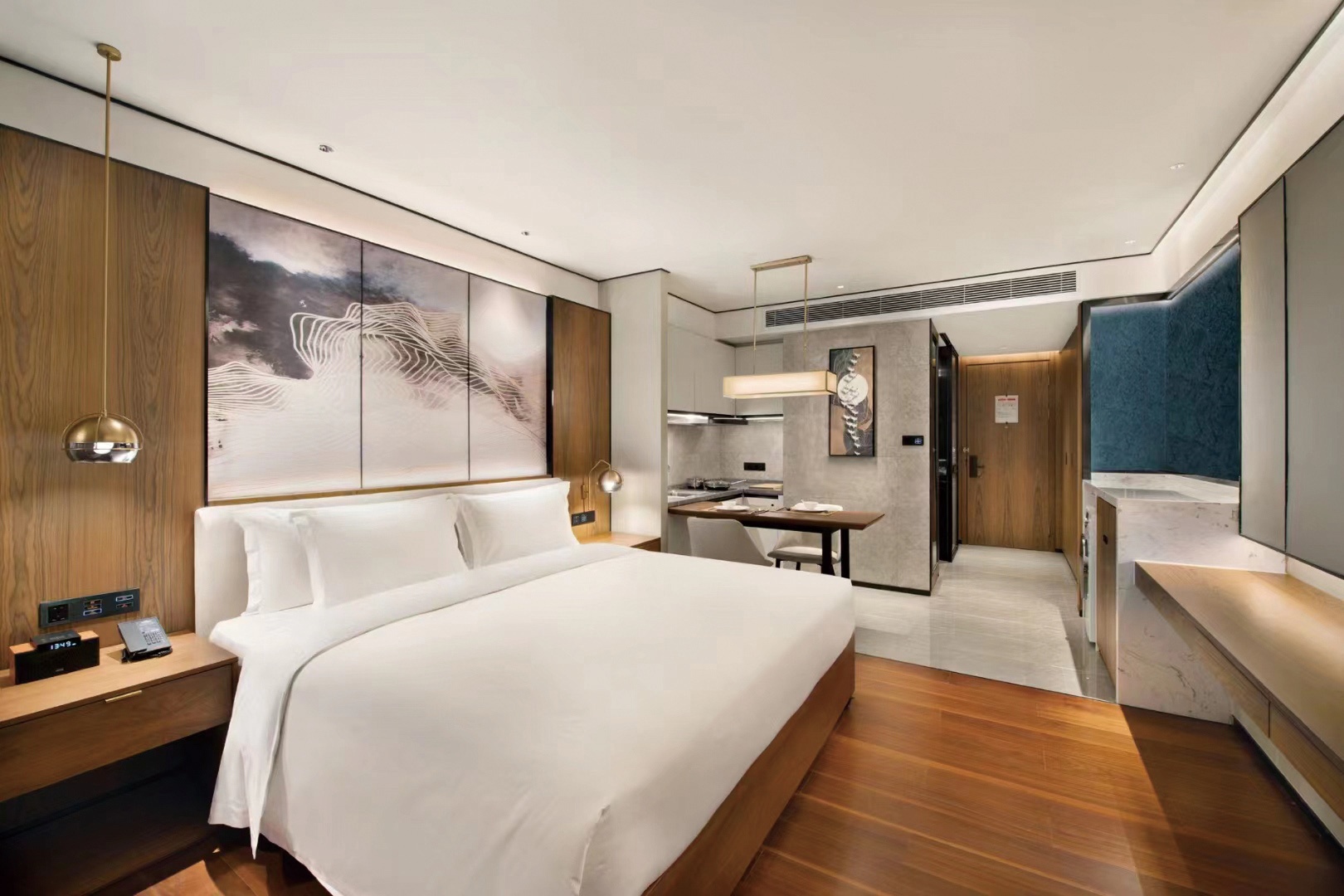 Modern hotel studio apartment with a double bed, wooden flooring, and integrated kitchenette area.