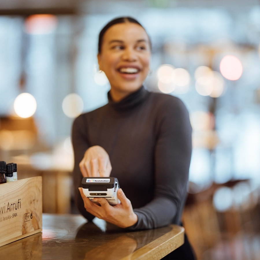 Smiling woman using a payment terminal to complete a transaction in a cozy setting.