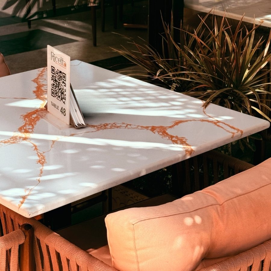 Table with QR code menu holder labeled Ricetta and table number 48 in a sunlit seating area.