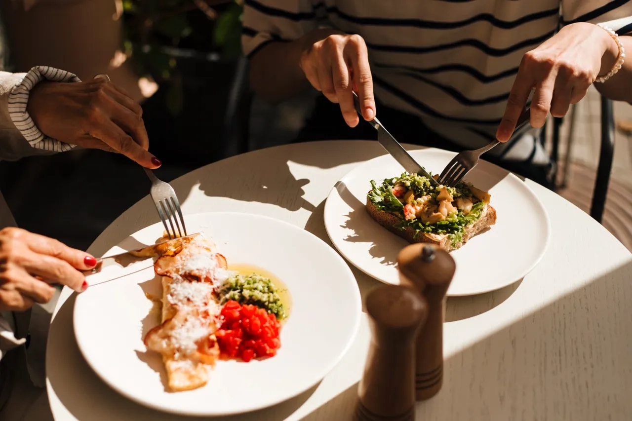 A man and woman sitting at a table enjoying a meal with plates of food and a glass of lemon water.