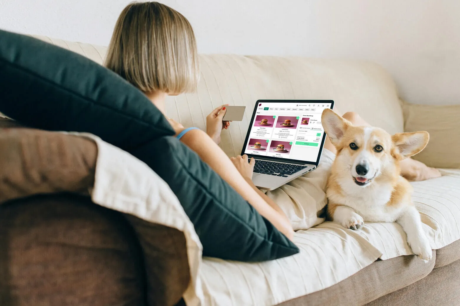 Frau sitzt am Computer auf der Couch, man sieht sie von hinten und auf dem Bildschirm den SIDES Webshop. Ein Hund sitzt neben ihr auf der Couch und schaut in die Kamera