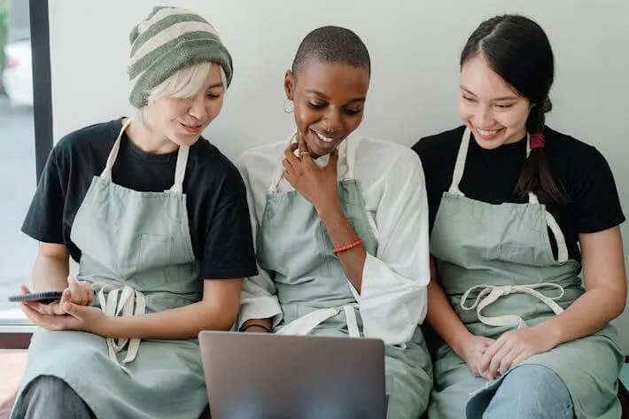 3 Kellnerinnen sitzen lächelnd vor dem Laptop