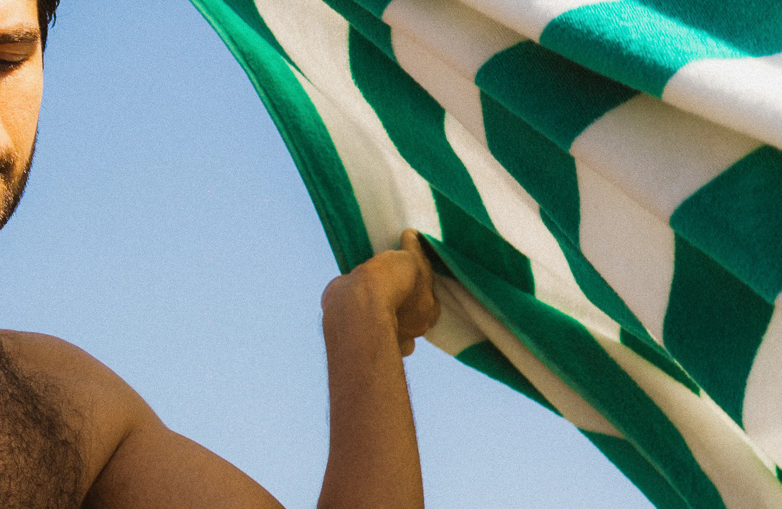 Un homme tenant une serviette rayée verte et blanche sur un fond de ciel bleu clair.
