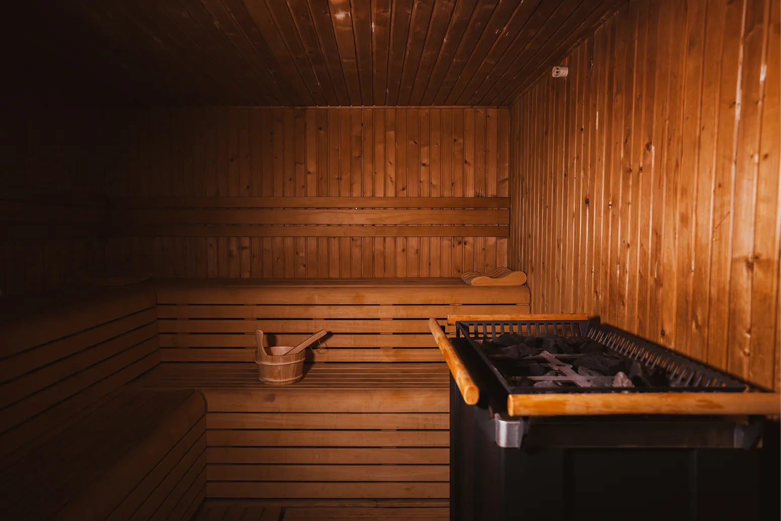 Intérieur d'un sauna en bois avec un seau en bois et une cuillère sur la banquette.