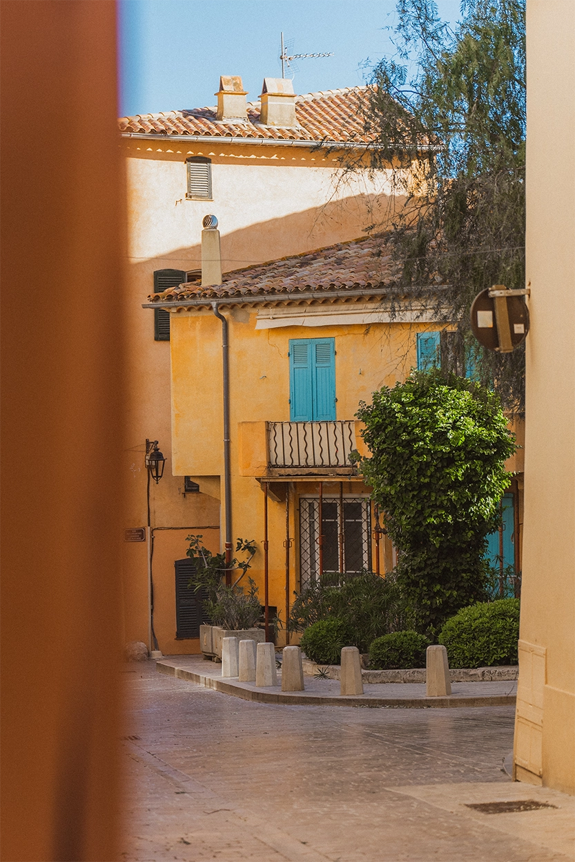 Ruelles pavées avec maisons jaunes et volets bleus sous un ciel bleu clair.
