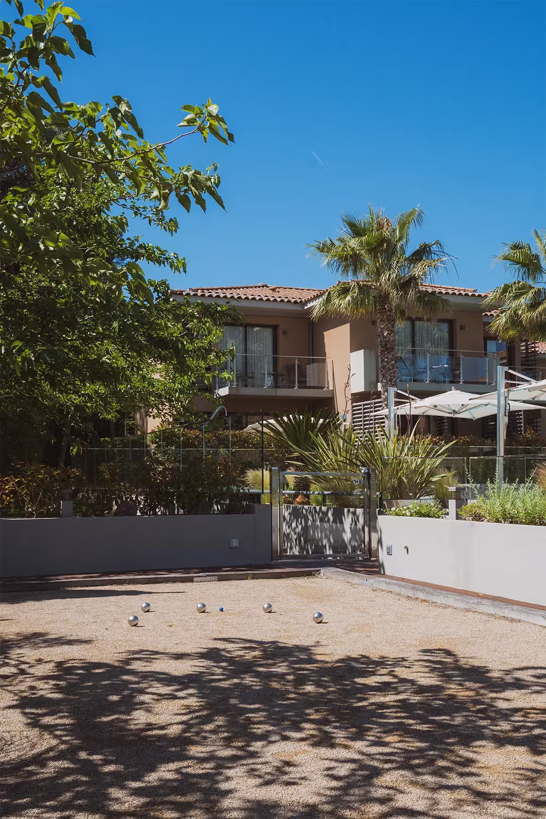 Terrain de pétanque devant un bâtiment résidentiel avec balcons, sous un ciel bleu clair.