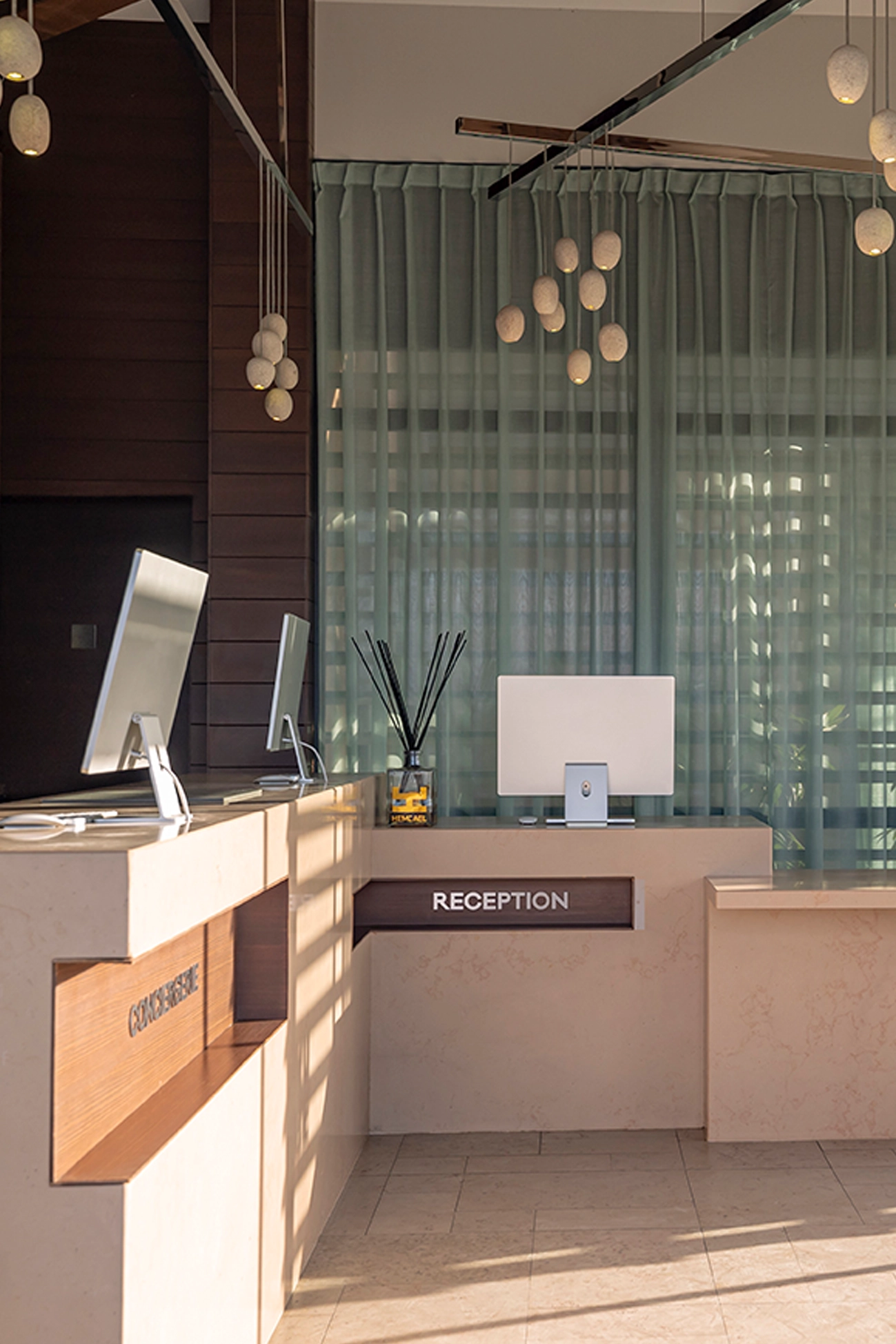 Comptoirs modernes de conciergerie et de réception avec ordinateurs et éclairage suspendu dans un espace lumineux.