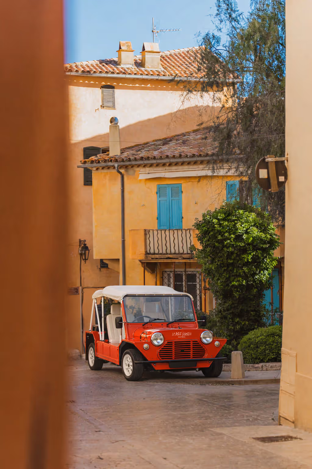 Petit véhicule rouge avec toit blanc garé dans une ruelle entre des maisons colorées.