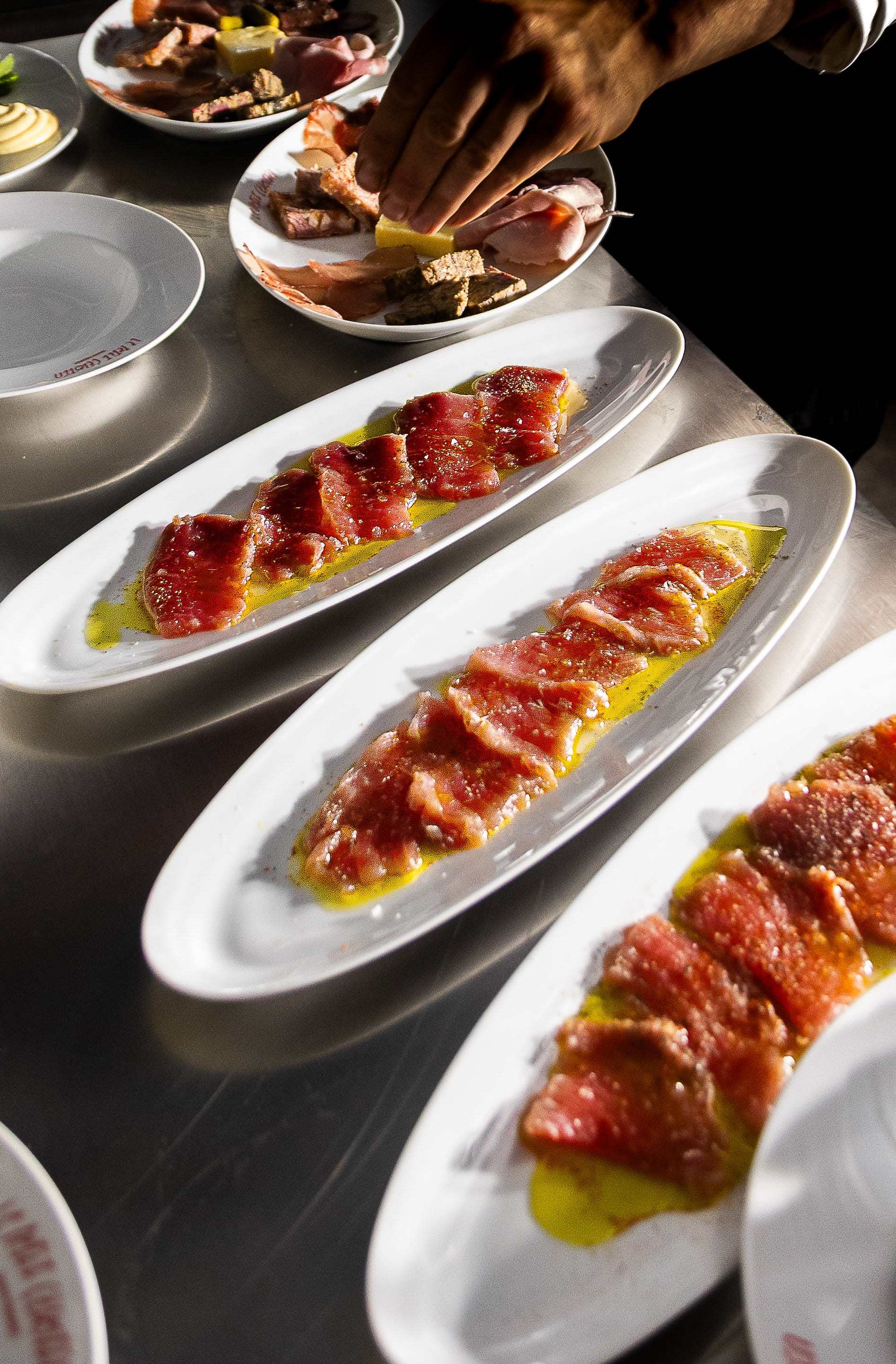 Tranches de viande crue assaisonnées avec de l'huile d'olive sur des assiettes blanches longues.