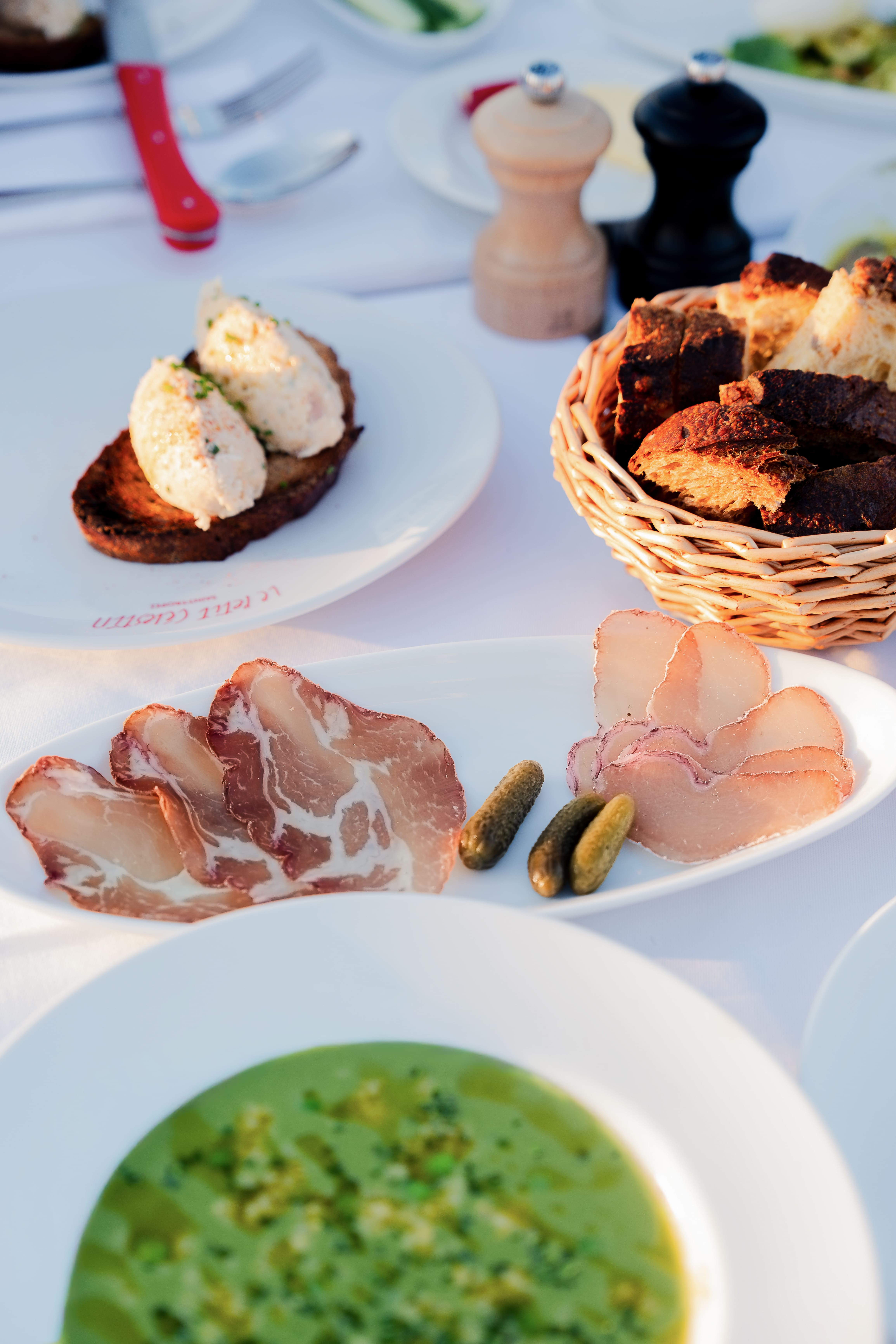 Assiette avec tranches de charcuterie et cornichons, soupe verte, pain et tartine avec mousse.
