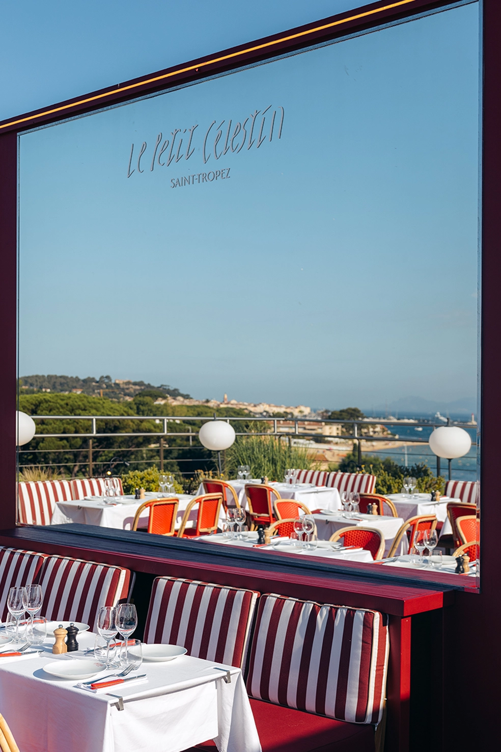 Terrasse de restaurant avec tables dressées, chaises rouges et vue sur paysage et mer à Saint-Tropez.