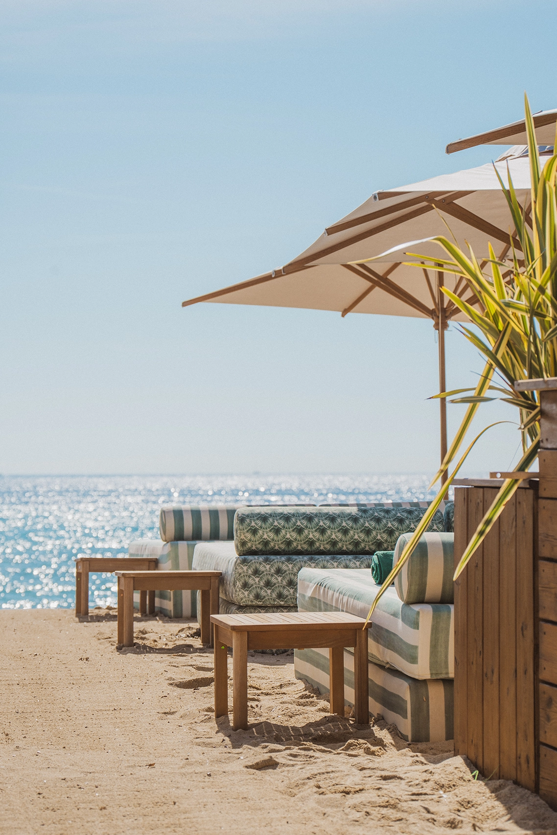 Espace lounge chic sur le sable de la Plage Cybelle à Ramatuelle, avec banquettes rayées, tables en bois et parasols face à la mer azur.