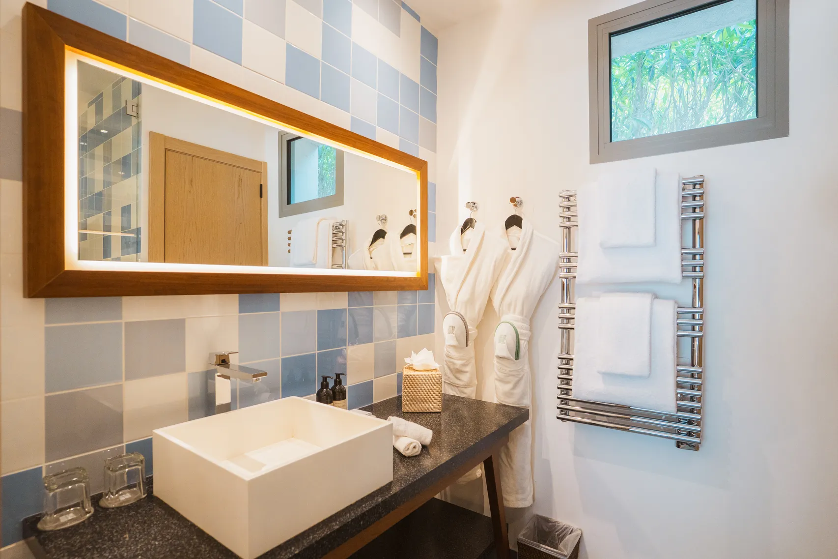 Salle de bain contemporaine avec vasque à poser blanche, grand miroir rectangulaire rétroéclairé et carrelage mural en mosaïque de tons bleus et gris.