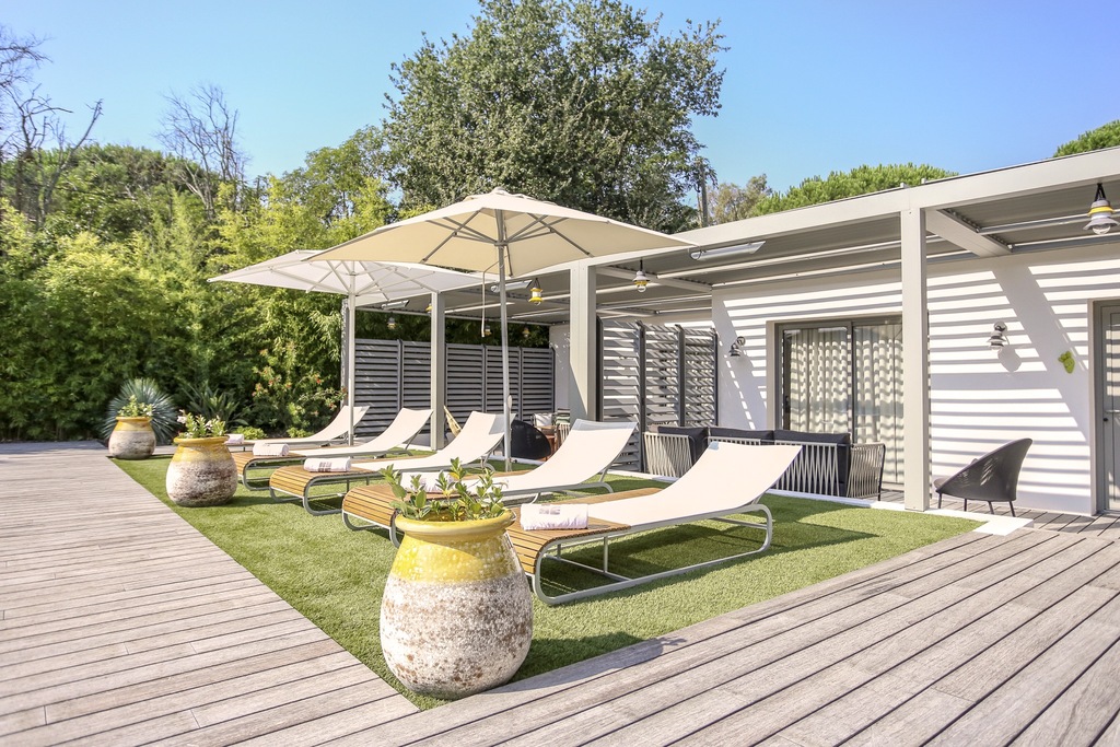 Espace détente extérieur style Ibiza avec transats design, parasols blancs et grandes jarres en céramique jaune en bord de piscine.