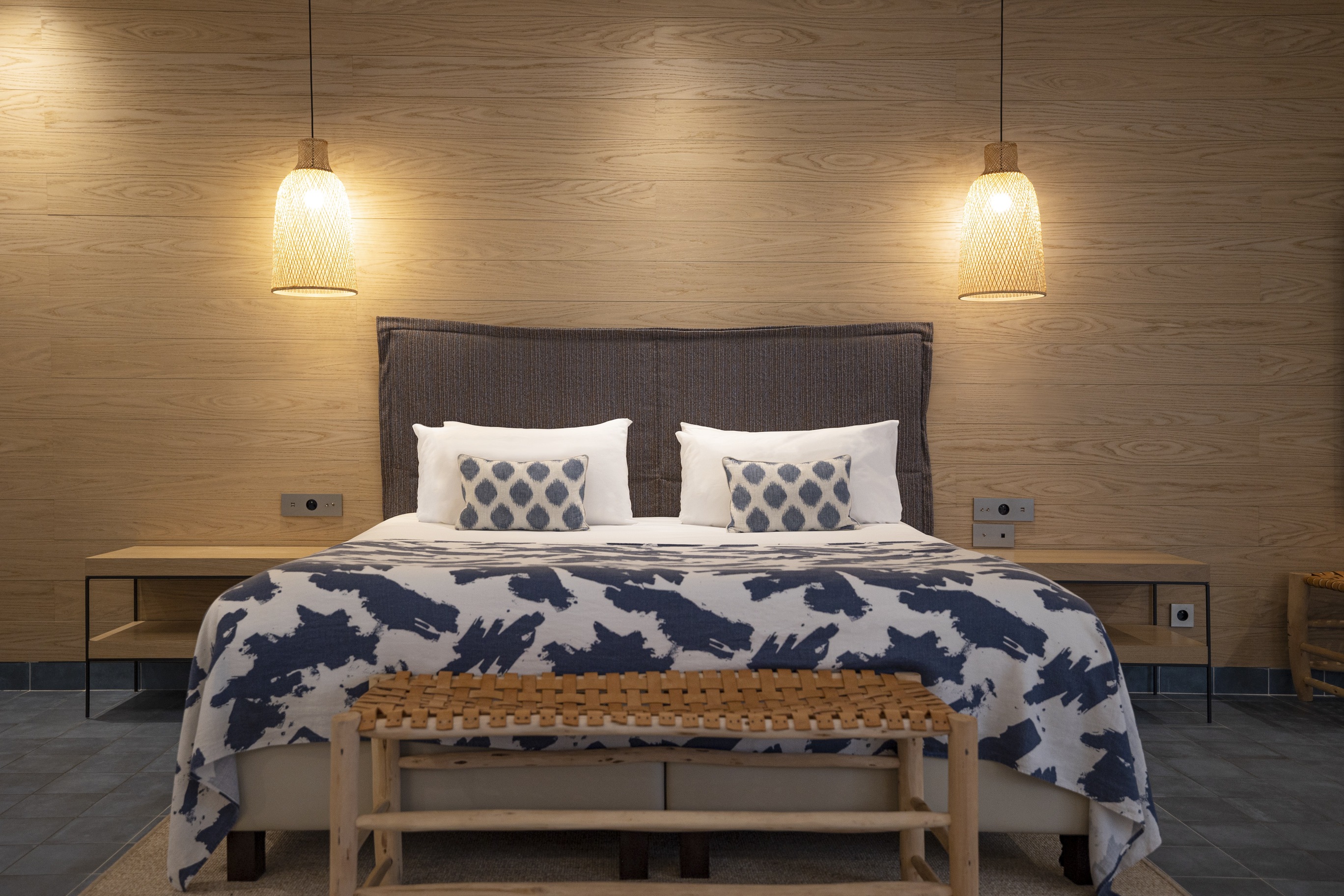 Lit king-size style Ibiza avec tête de lit en bois naturel, suspensions lumineuses tressées et textile de lit aux motifs organiques.