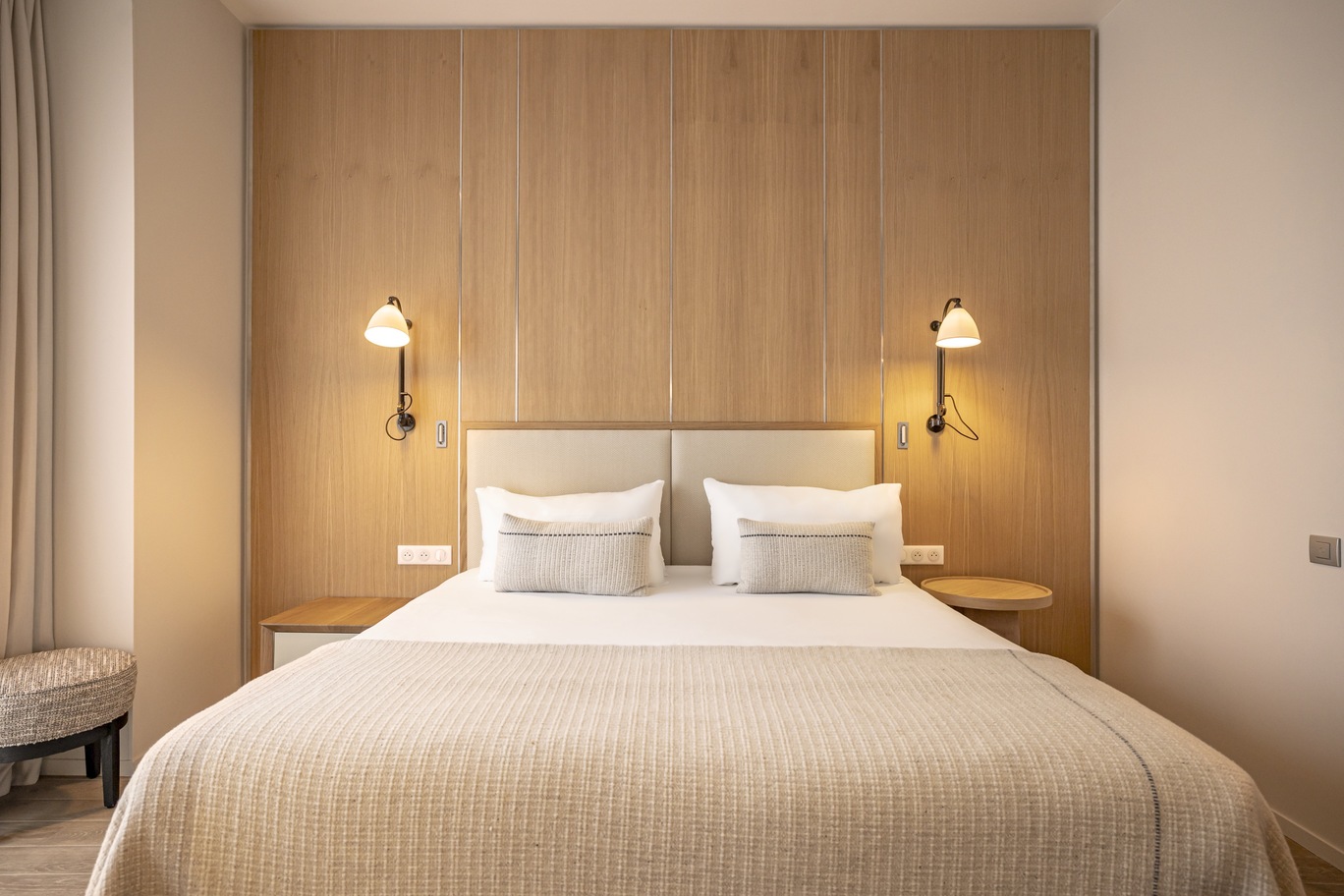 Chambre au design naturel avec tête de lit monumentale en bois clair, appliques murales vintage et linge de lit blanc épuré.