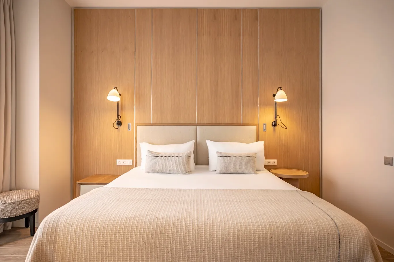 Chambre au design naturel avec tête de lit monumentale en bois clair, appliques murales vintage et linge de lit blanc épuré.