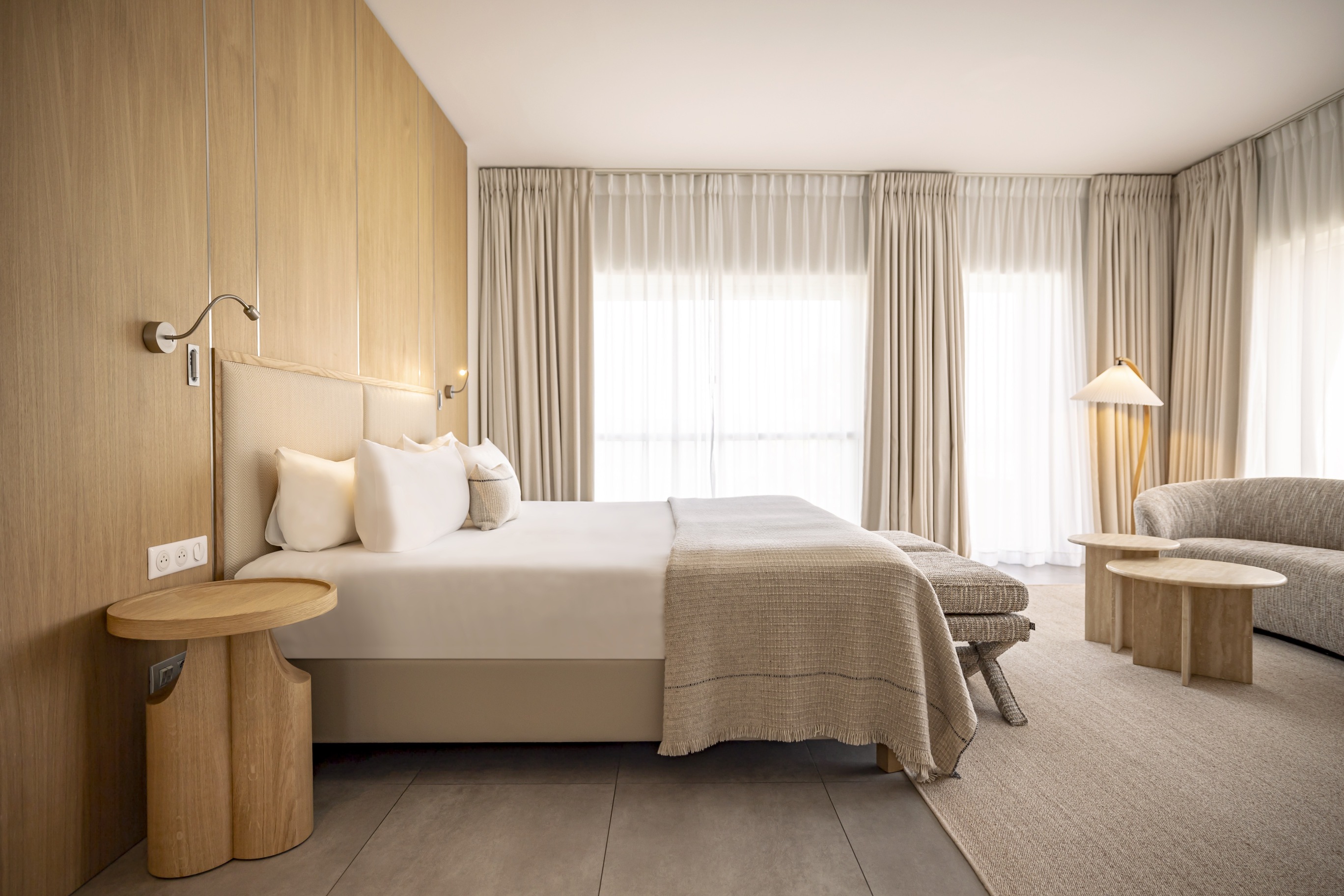 Espace détente de la Suite Junior avec canapé incurvé aux lignes organiques, tables basses en bois et luminaire design