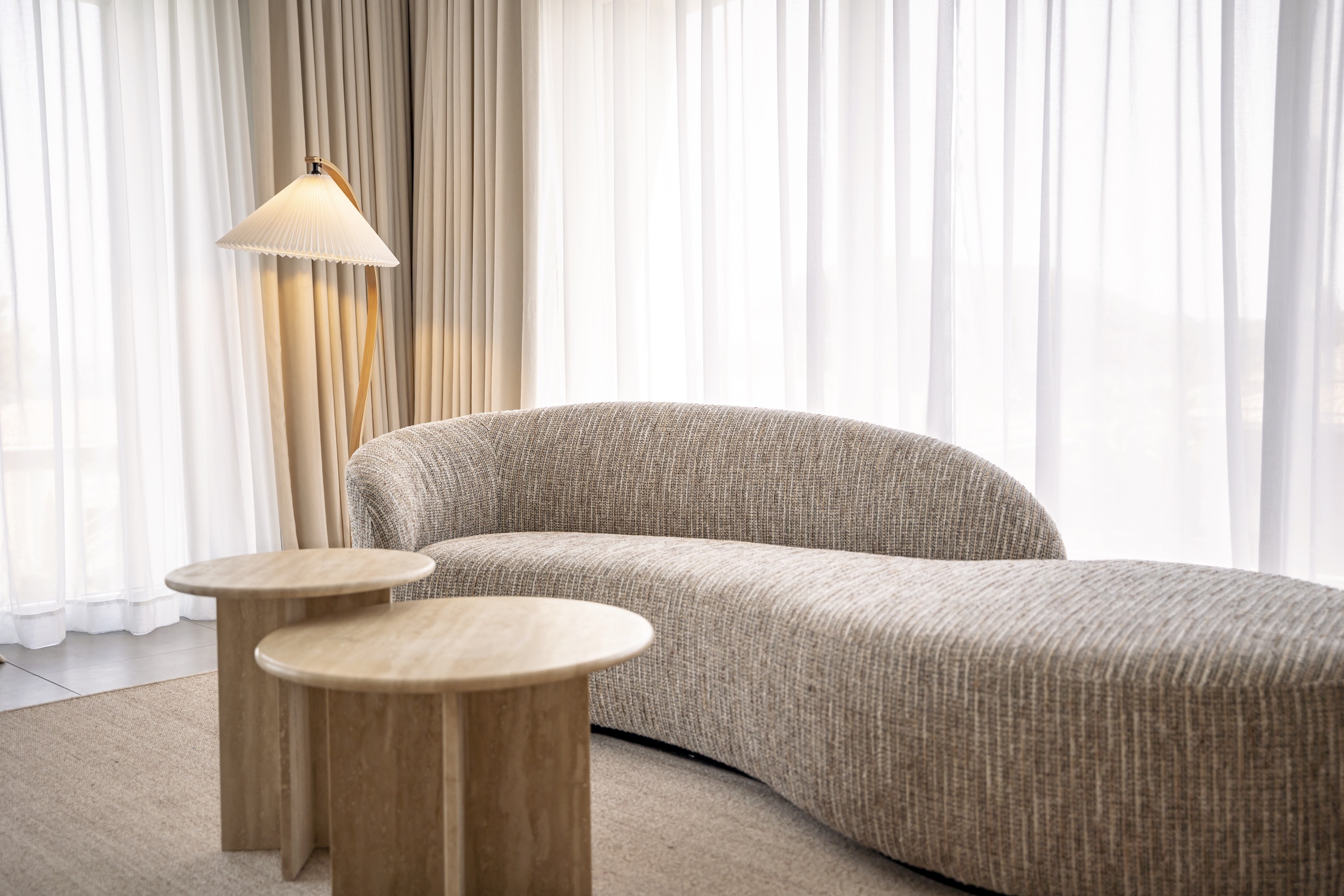 Espace détente de la Suite Junior avec canapé incurvé aux lignes organiques, tables basses en bois et luminaire design