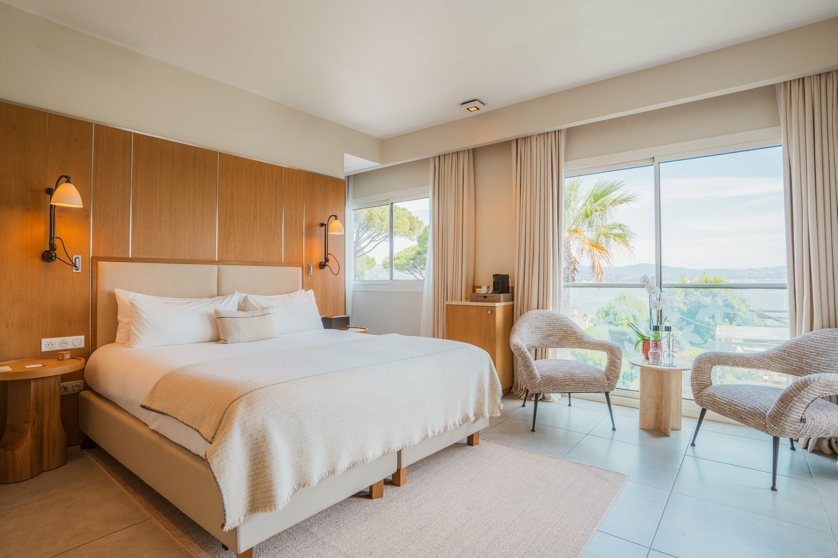 Chambre de luxe vue mer avec grand lit douillet, finitions en bois massif et fenêtre ouvrant sur le littoral méditerranéen.