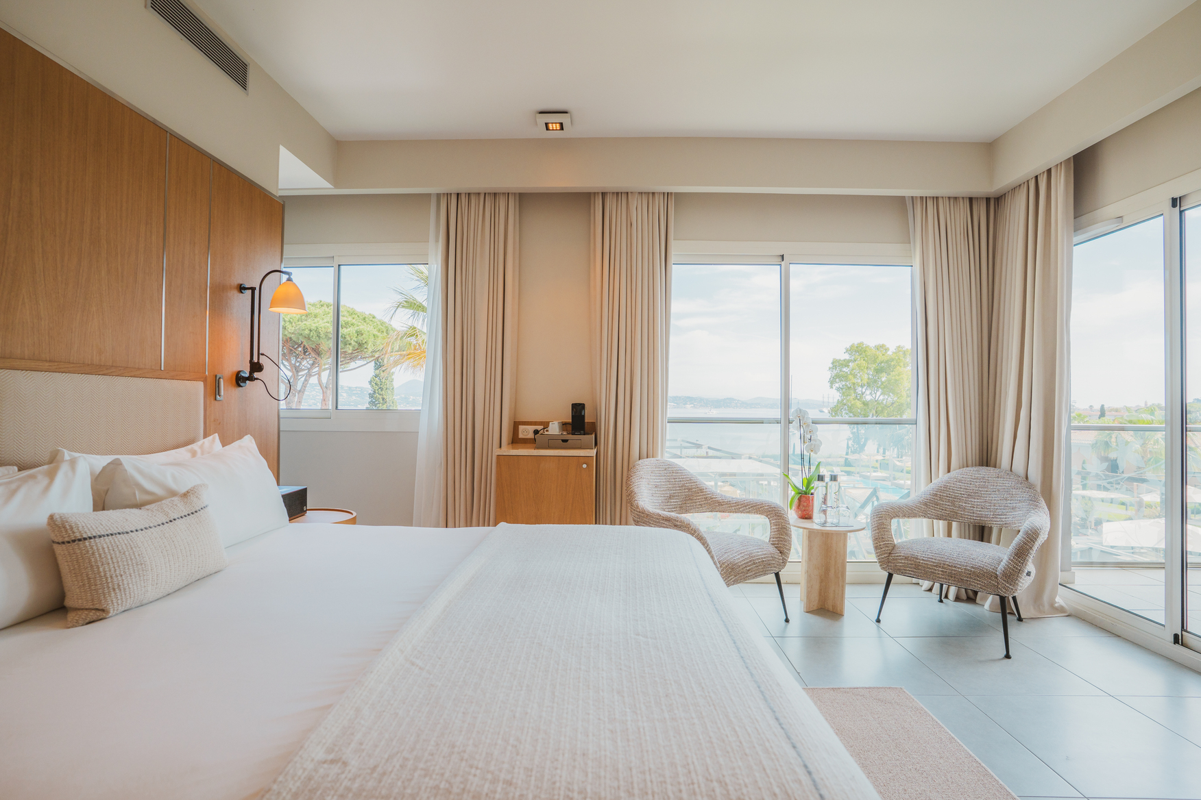 Chambre de luxe vue mer avec grand lit douillet, finitions en bois massif et fenêtre ouvrant sur le littoral méditerranéen.