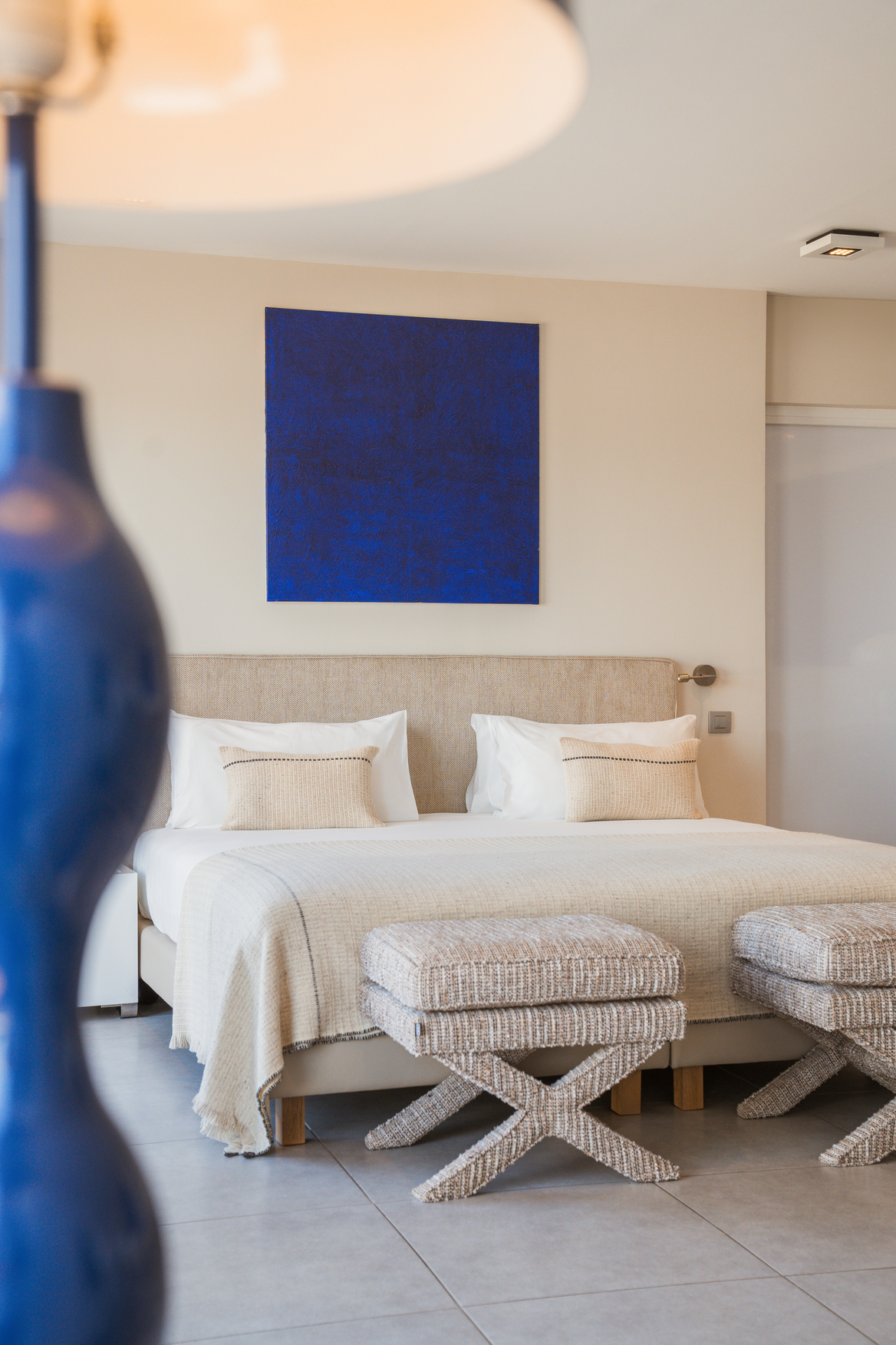 Suite de luxe Natural Sea avec lit king-size, décoration minimaliste ponctuée de bleu cobalt et grandes baies vitrées ouvrant sur la mer.