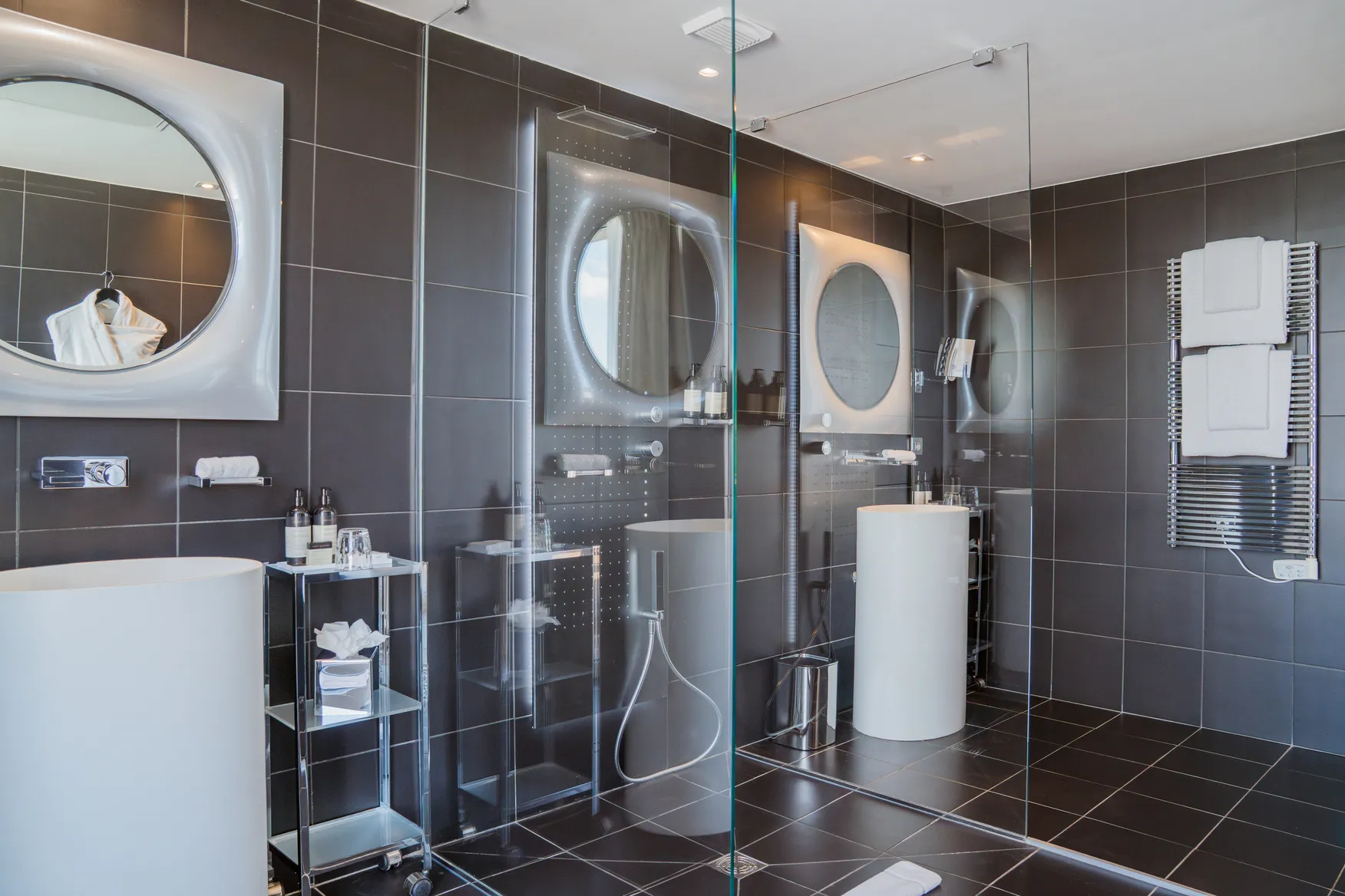 Salle de bain de standing avec double vasque totem, miroirs ronds design et douche à l'italienne moderne.
