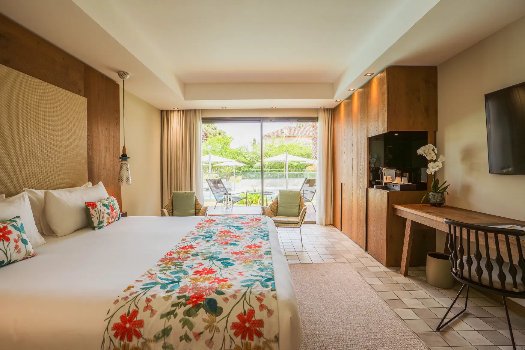 Chambre Deluxe avec grandes baies vitrées ouvrant sur une terrasse privée, mobilier en bois naturel et vue sur les jardins de l'hôtel.