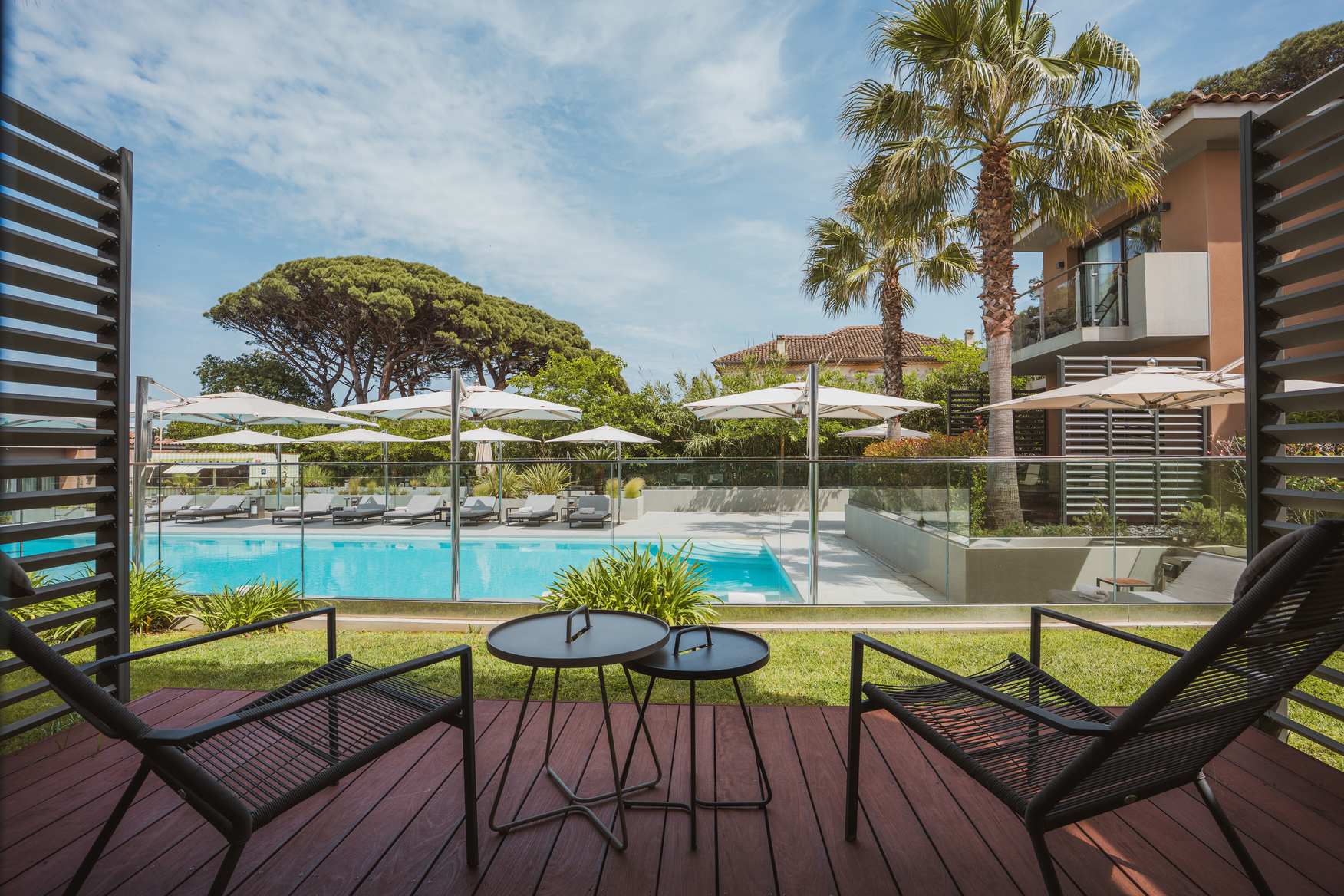 Terrasse privée de la chambre Deluxe Wood avec salon de jardin en métal noir, vue directe sur la piscine et les palmiers.