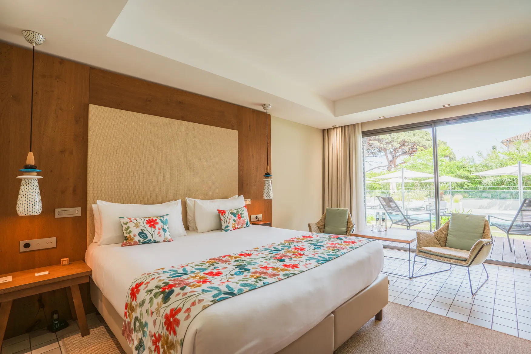 Chambre Deluxe Wood avec tête de lit monumentale en bois massif, jeté de lit floral coloré et ambiance lumineuse chaleureuse.