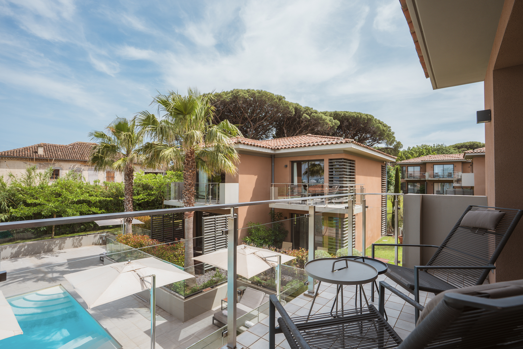 Espace détente extérieur style Ibiza avec transats design, parasols blancs et grandes jarres en céramique jaune en bord de piscine.